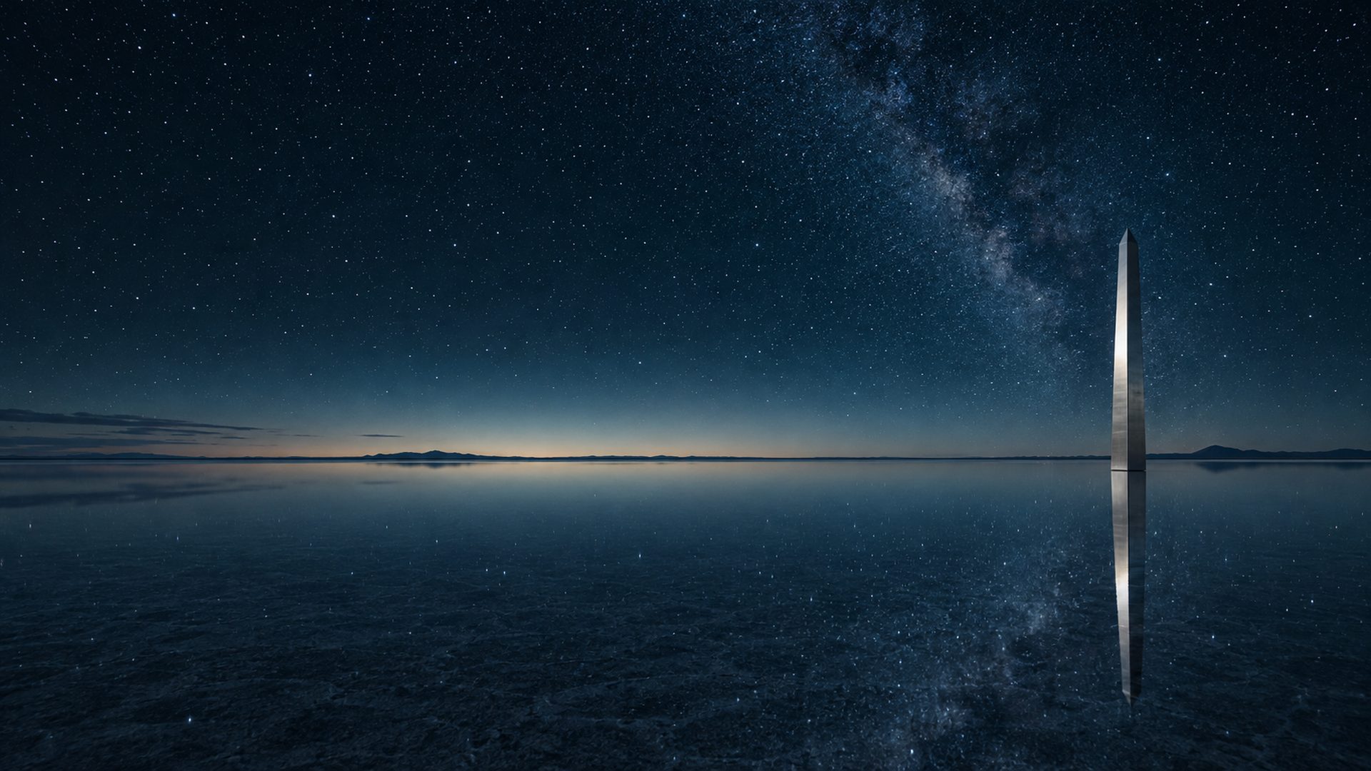 A slender silver monolith reflected in a star-filled salt lake